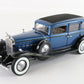 A vintage-style blue model car with black fenders, black roof, white-walled tires, and chrome details, photographed on a plain light background.
