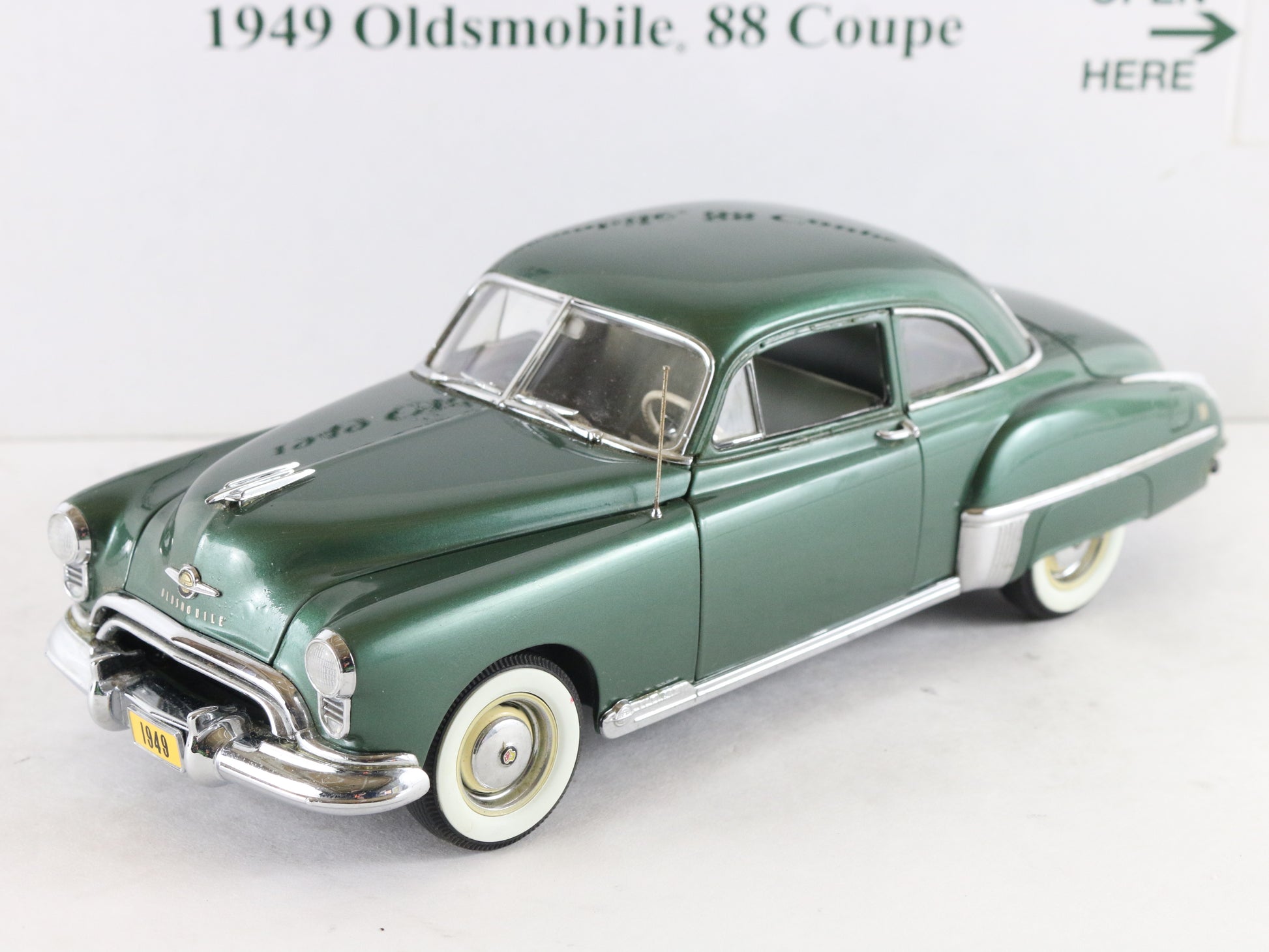 A green vintage die-cast model car with chrome details and white-walled tires, photographed against a plain white background with text partially visible above.