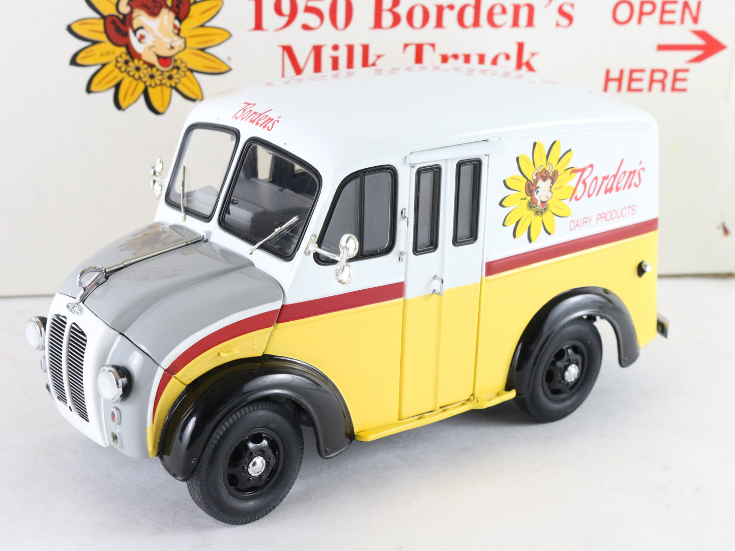 A vintage Borden's Dairy Products milk truck model, featuring a white upper body, yellow lower body, a gray hood, and red stripes, displayed against a themed background with a vintage sign.