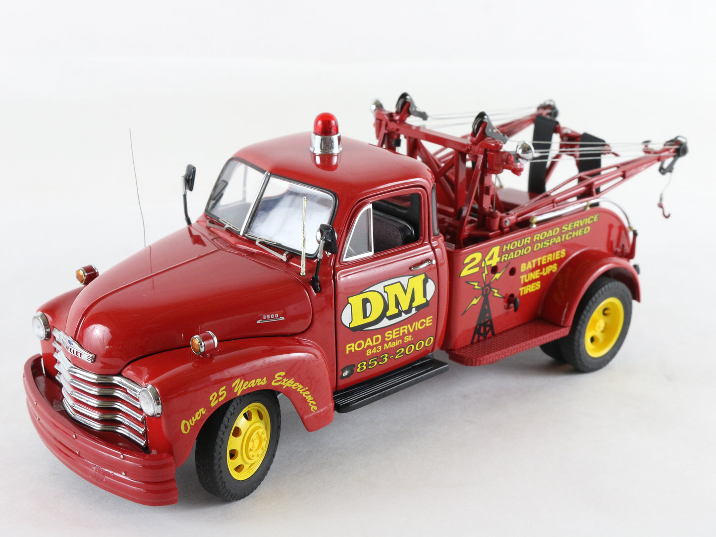 A red vintage tow truck model with yellow wheels, featuring 'DM Road Service' graphics and a red light on top, photographed on a white background.