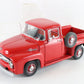 A red vintage Ford pickup truck model, photographed on a clean white background. The model features a clear windshield, chrome details, and a spare tire mounted on the side.