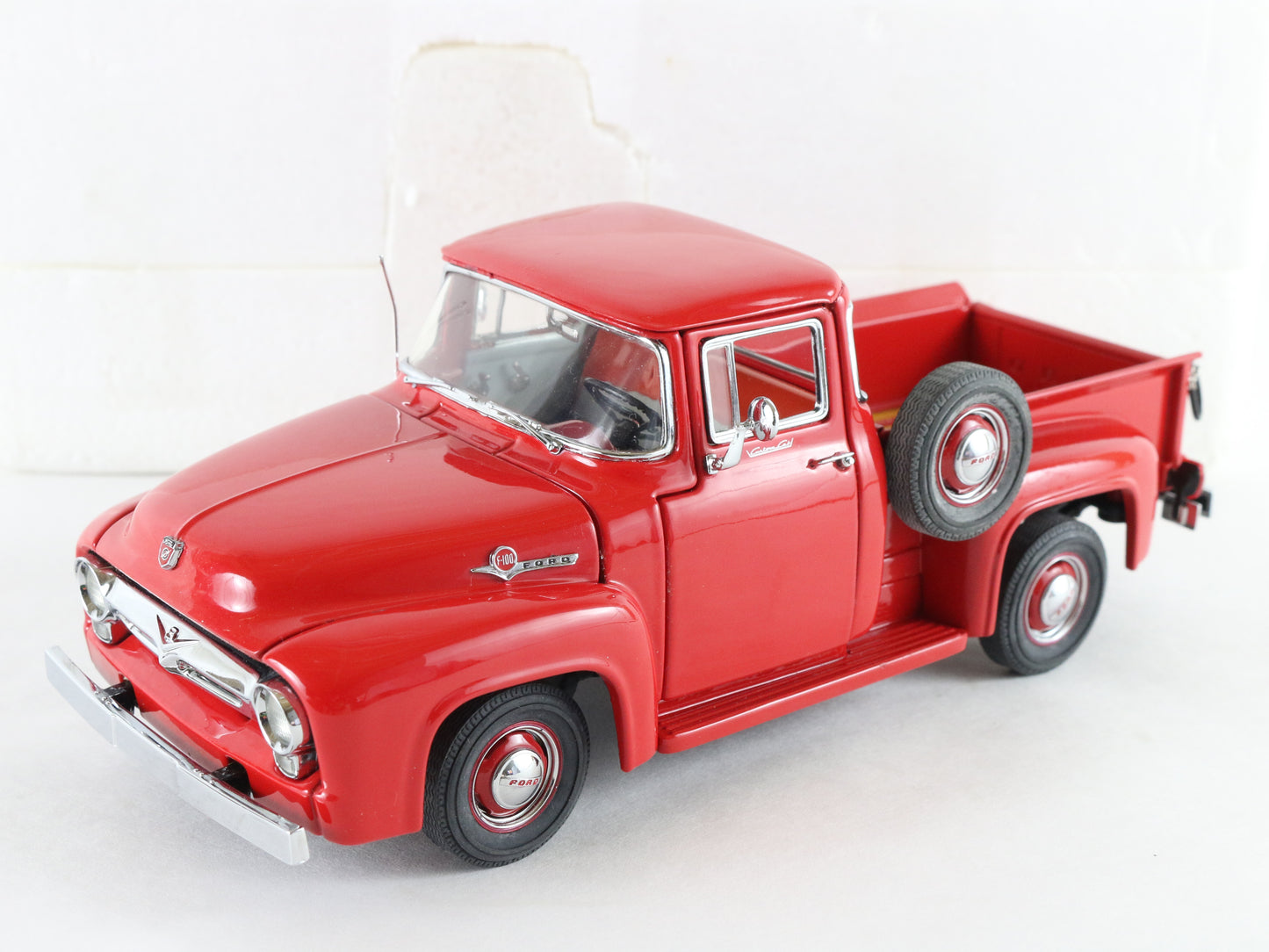 A red vintage Ford pickup truck model, photographed on a clean white background. The model features a clear windshield, chrome details, and a spare tire mounted on the side.