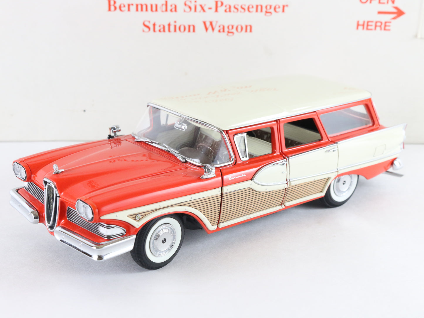 A vintage-style model station wagon toy car in red, cream, and tan, photographed on a plain white background with printed red text above.