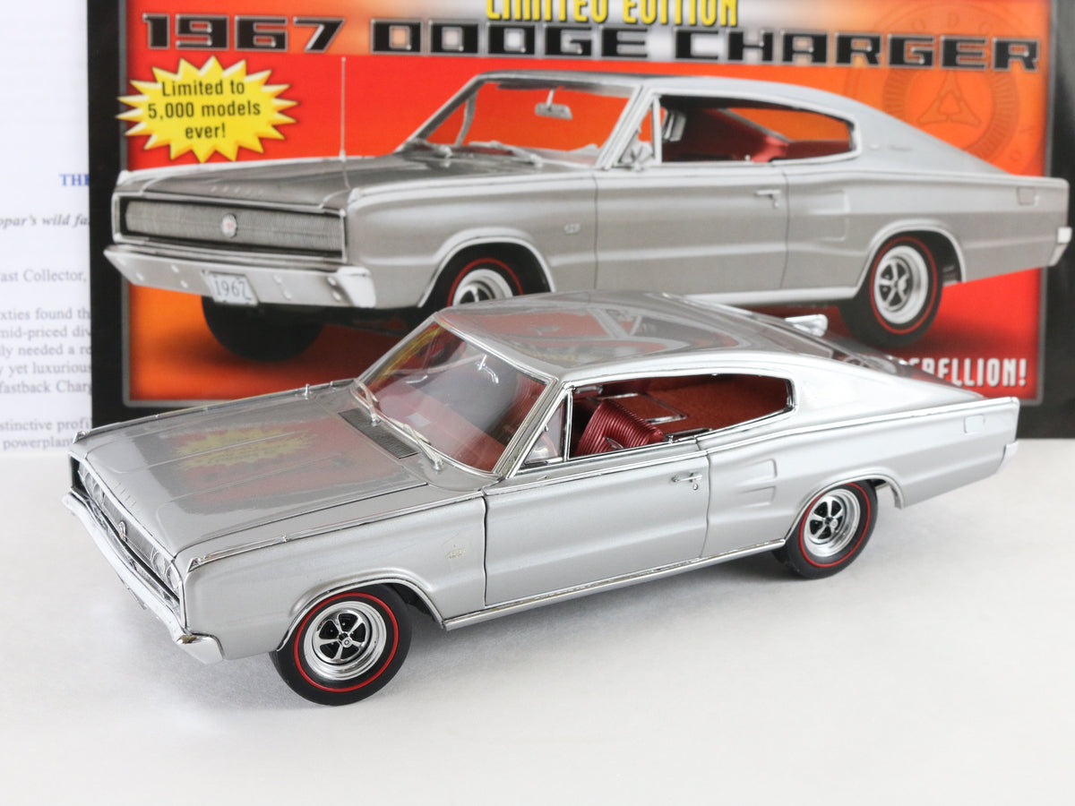 A silver die-cast model car of a 1967 Dodge Charger with red interior and black-and-red wheels, shown in front of its original orange and red packaging box.