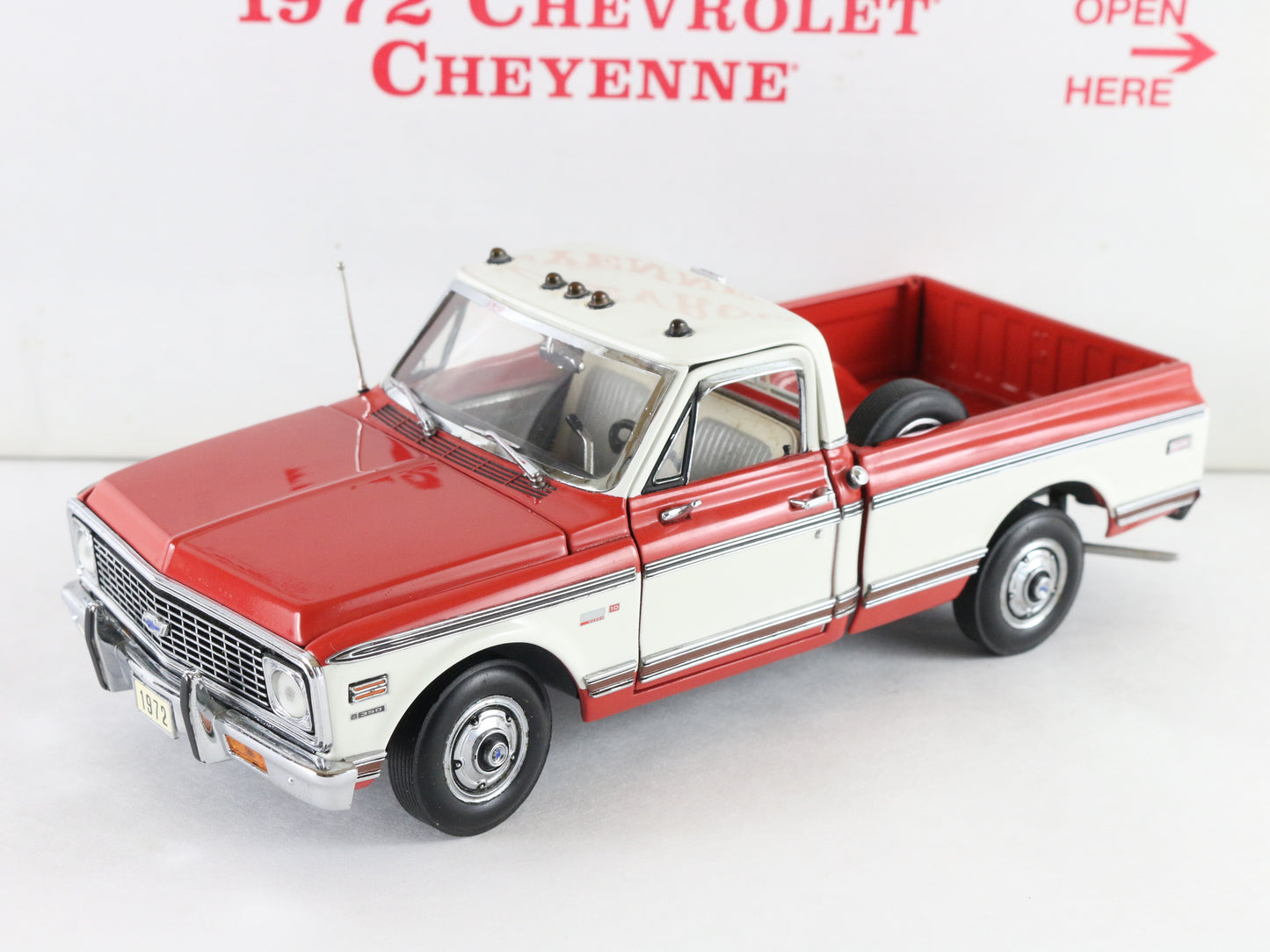 A 1972 Chevrolet Cheyenne model truck in a red and white color scheme, displayed on a white background with a sign reading '1972 CHEVROLET CHEYENNE' and 'OPEN HERE'.